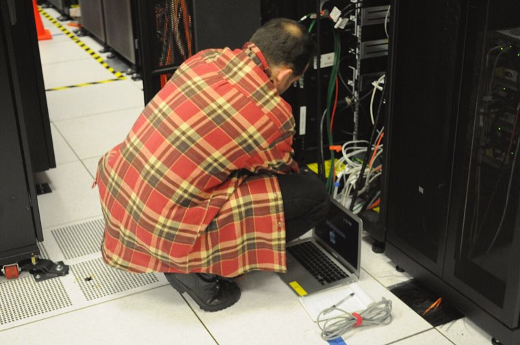 Technician crouching in front of a server rack, a laptop on the floor, in a computer room