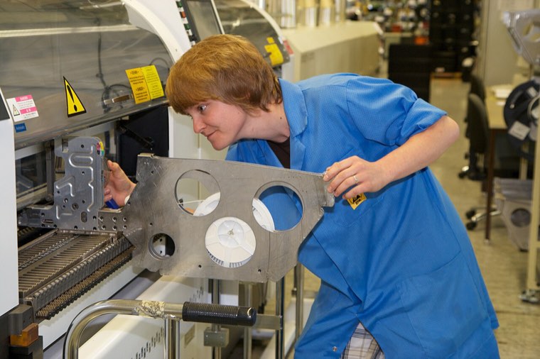 Production employee in a blue coat adjusting a part on an electronic component assembly machine in a German factory